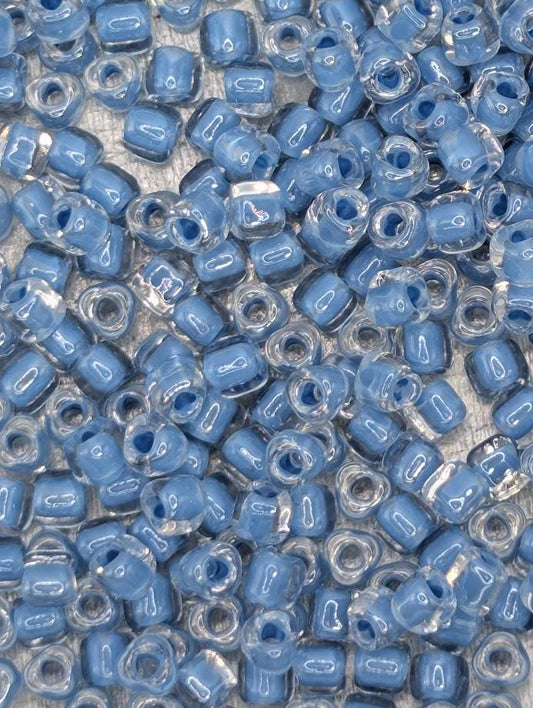 The image is a close-up of numerous small, clear beads in various shades of blue, scattered across a surface.
