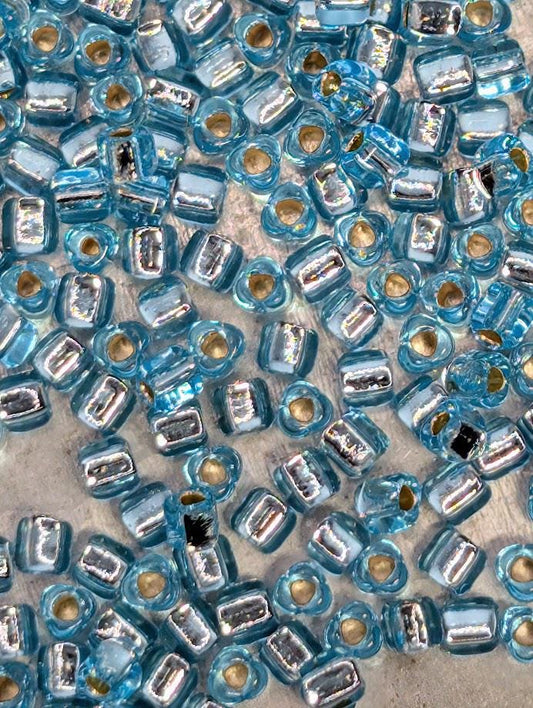 The image is a close-up of numerous blue and silver glass beads scattered across a surface.