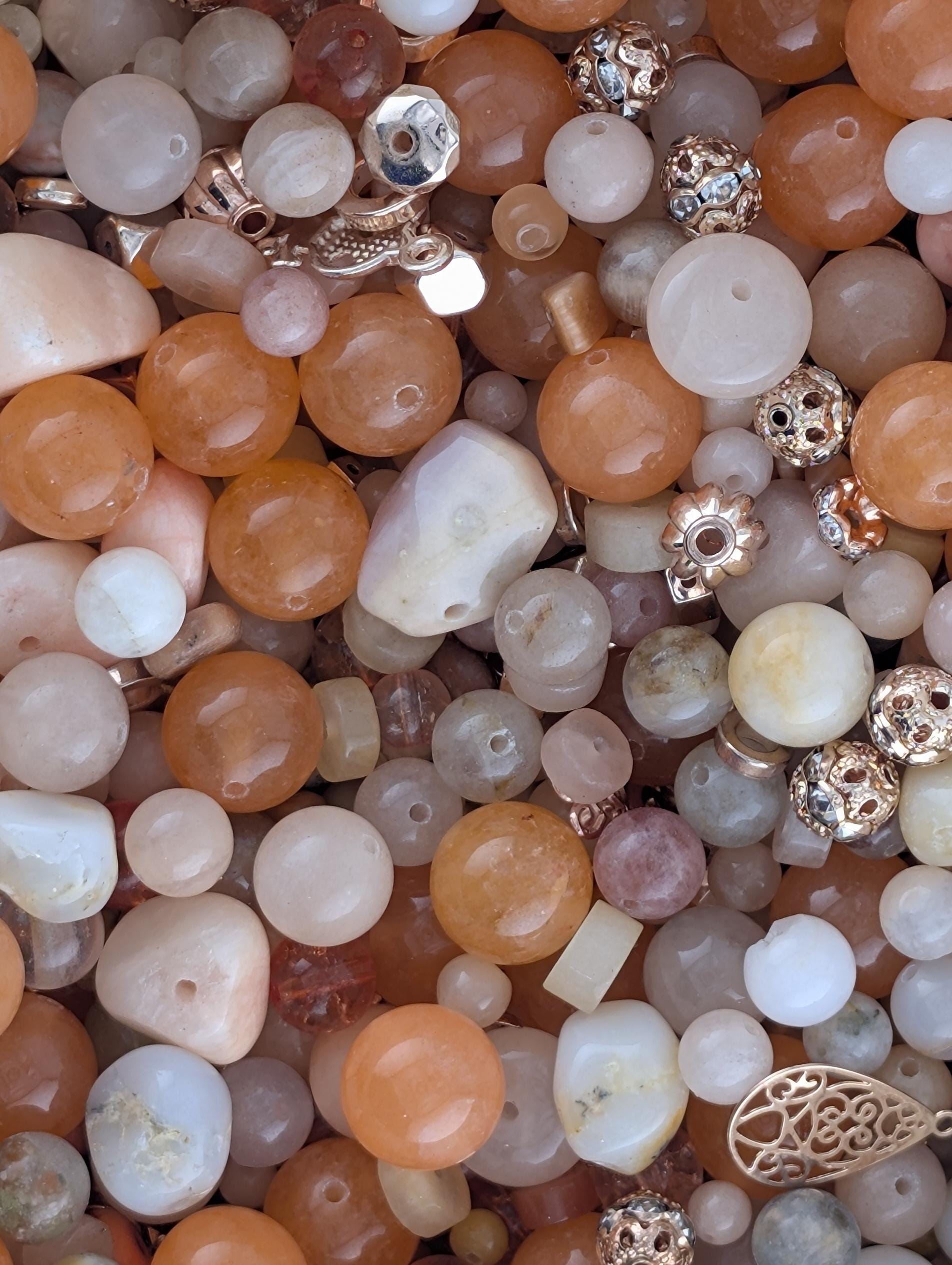 The image is a close-up of various beads and jewelry pieces, including beads in shades of orange, white, and gold, as well as some with intricate designs.
