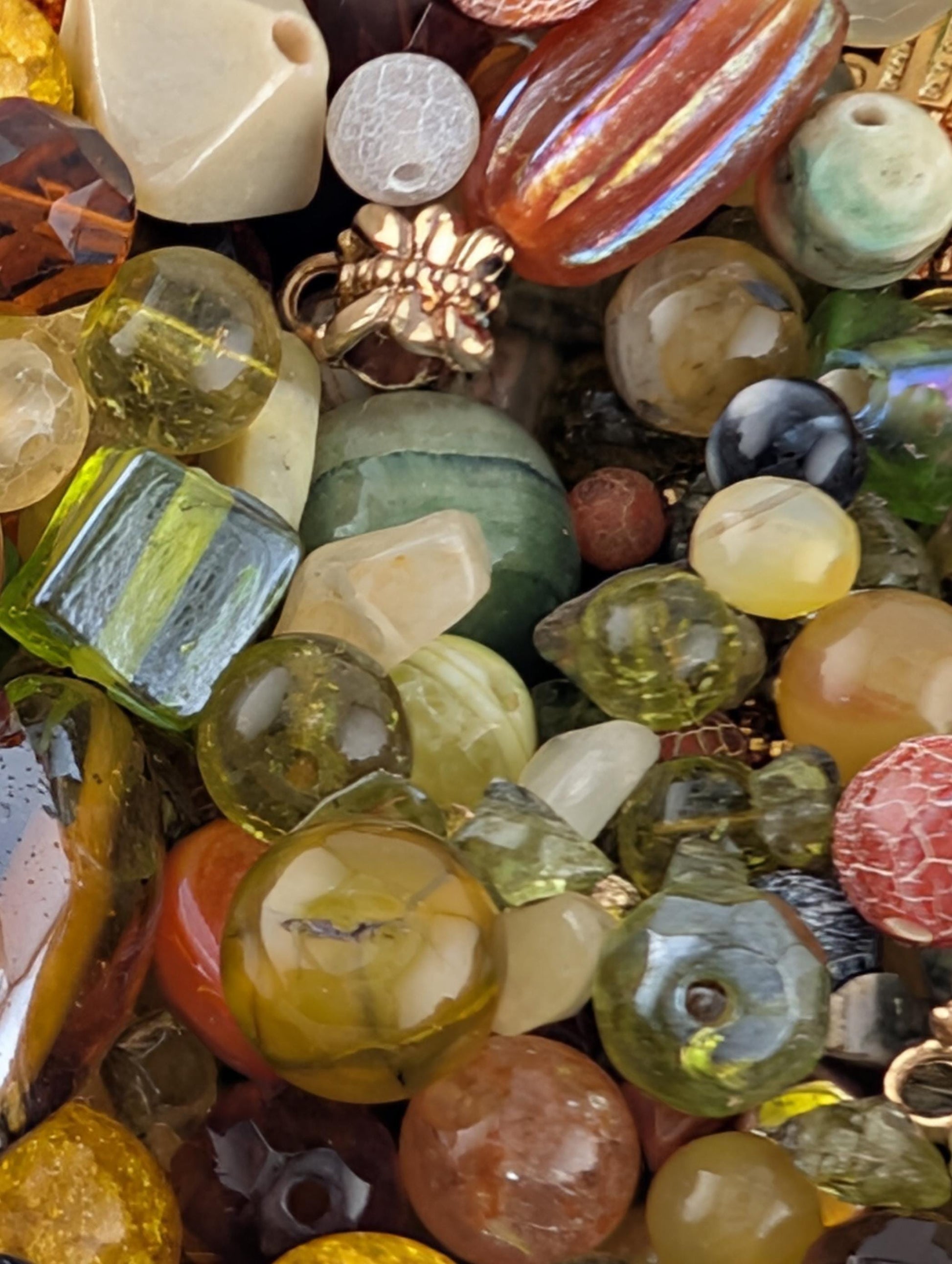 The image is a close-up of a collection of various colorful beads, gemstones, and glass objects.