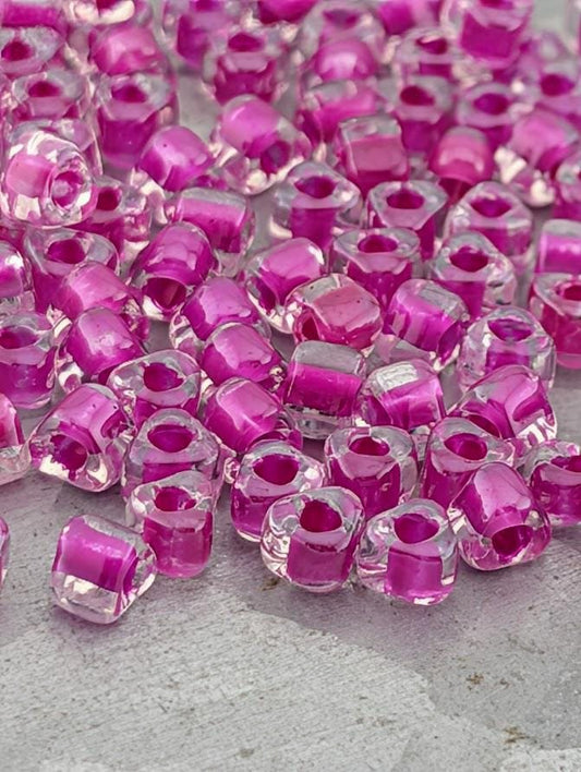 a close-up view of numerous clear glass beads in shades of pink and purple, scattered across a surface.