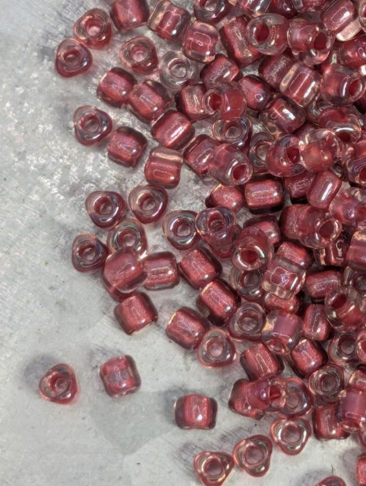 a collection of small, clear beads in various shades of red, scattered on a textured surface.