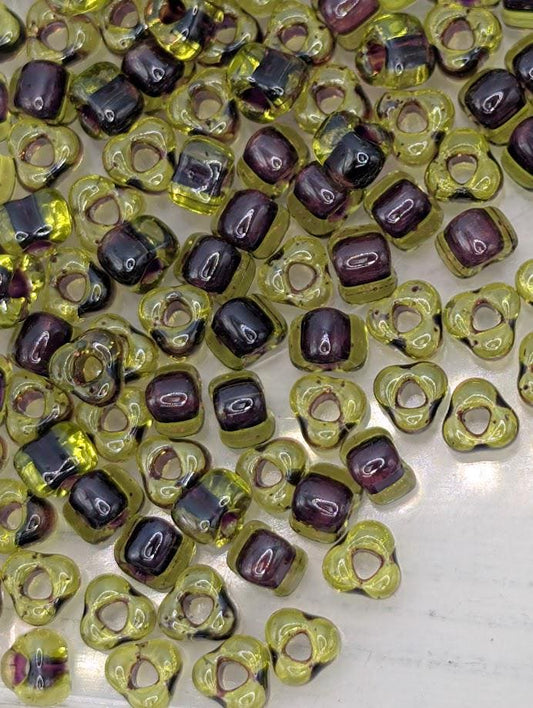a collection of small, colorful beads in various shades of green and purple, scattered across a surface.