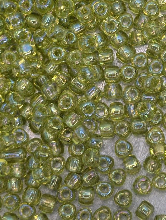 The image is a close-up of numerous small, clear beads in various shades of green. The beads are scattered across a surface, creating a visually interesting and vibrant display.