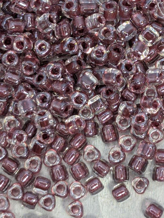 The image is a close-up of numerous small, clear beads in various shades of purple, scattered across a surface.