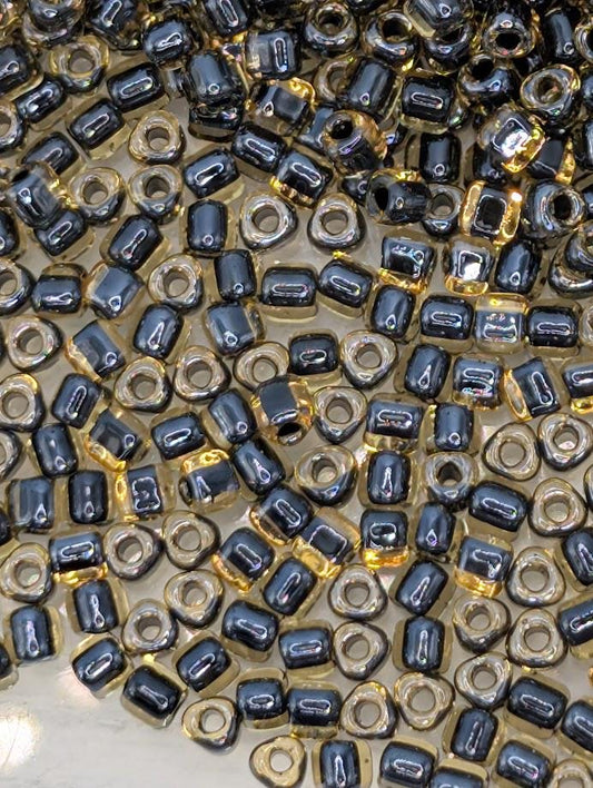 a close-up view of numerous small, round beads in various shades of black and gold. The beads are scattered across the frame, creating a visually striking and intricate pattern.