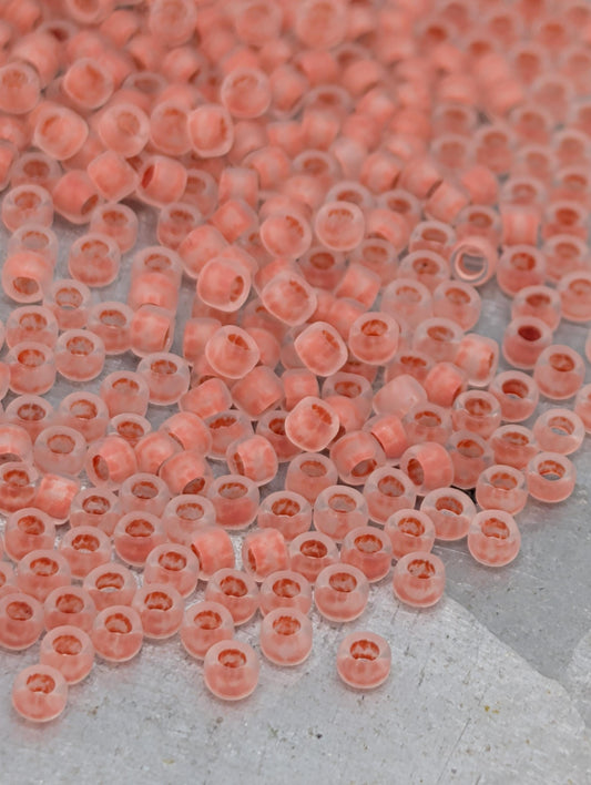 a large number of small, clear beads in shades of pink and orange, scattered across a surface.