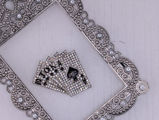 A silver ornate frame with a diamond-encrusted border, and a set of playing cards with a black back and white front resting on a white surface.