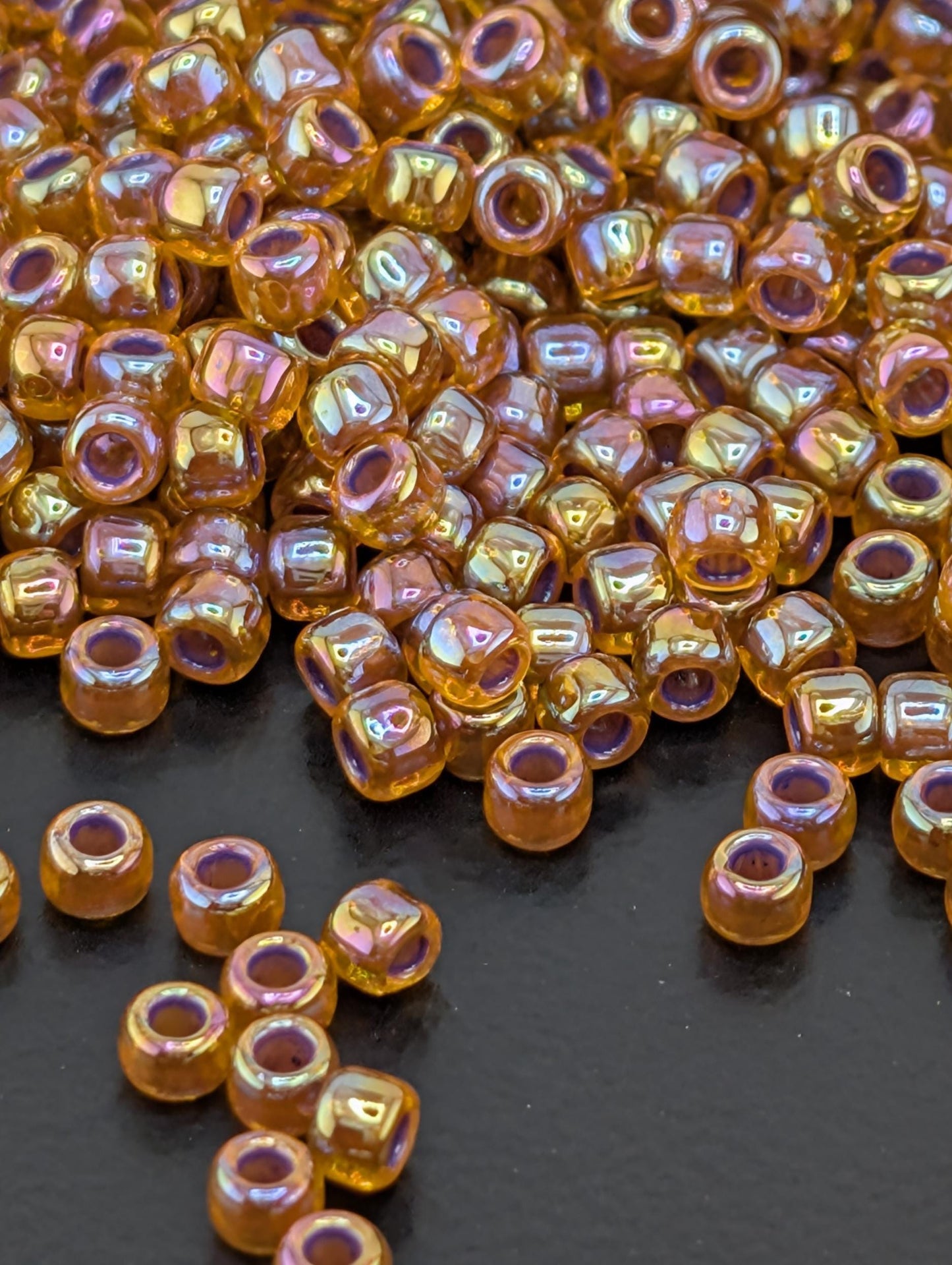 a close-up view of numerous small, round beads scattered on a dark surface. The beads have a shiny, metallic appearance and are of various colors, creating a visually striking and vibrant display.